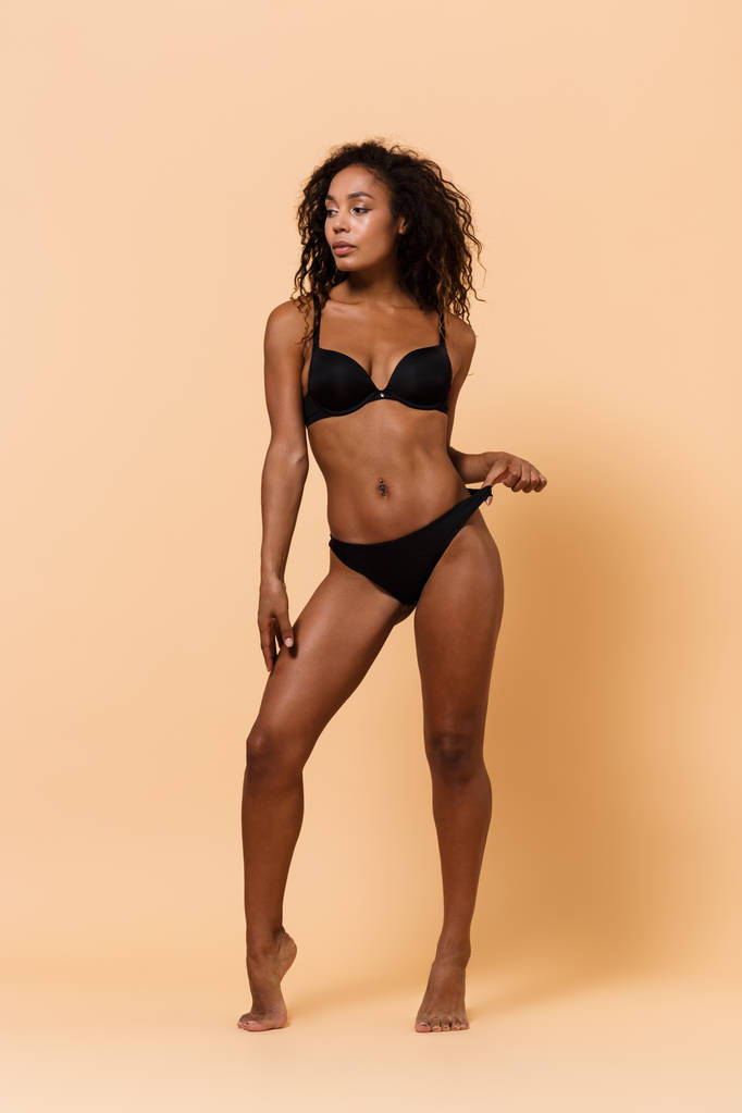 Bej renkli arka plan üzerinde izole ayakta Afro-Amerikan Kız 20'li yaşlarda giyen siyah iç çamaşırı Güzellik Portresi - Fotoğraf, Görsel