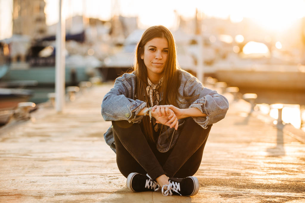 Jovem bela mulher sentada no porto marítimo ao sol
 - Foto, Imagem