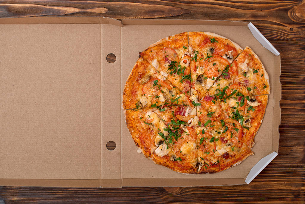 Pizza italiana saborosa na caixa em uma mesa de madeira.Entrega de pizza.Vista superior. Espaço de cópia
. - Foto, Imagem