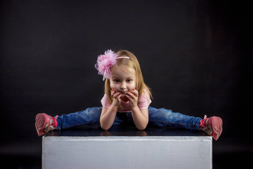 Portrait of cute European little blonde girls in jeans and pink t-shirt with the inscription: "Dad's pride, mom's joy", on a black isolated background - Photo, Image