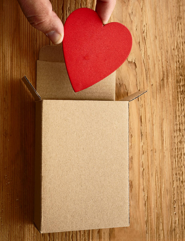 męskiej ręki trzymającej jedno serce czerwone powyżej otwarte pudełko na podłoże drewniane. Happy Valentines day. 14 lutego.    - Zdjęcie, obraz