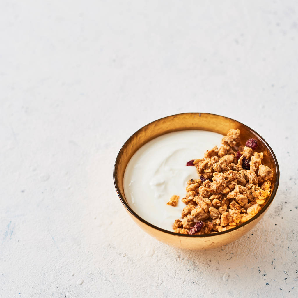 Healthy breakfast. Muesli with yogurt and honey in golden bowl on white abstract background. Top view. Square crop. Copy space for text. - Photo, Image
