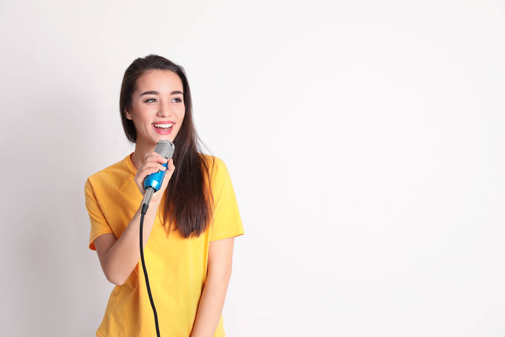 Молода жінка в повсякденному одязі позує з мікрофоном на кольоровому фоні. Простір для тексту
 - Фото, зображення