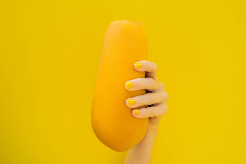 El ile turuncu olgun yemişi sarı bir arka plan üzerinde tutan sarı manikür - Fotoğraf, Görsel