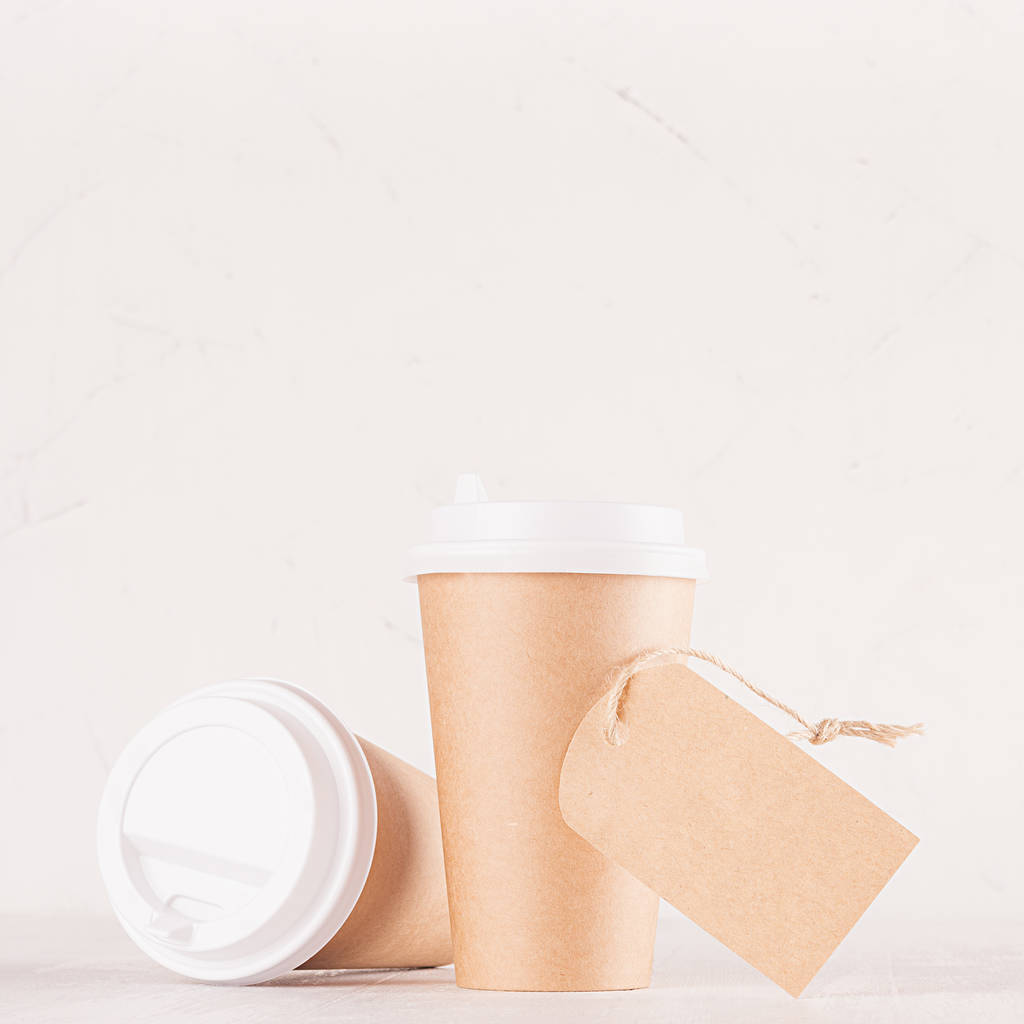 Макет для упаковки кави - дві чашки коричневого паперу ремесел, чисті білі шапки та чиста етикетка крупним планом на дошці з білого дерева, інтер'єр кафе. Сучасна елегантна концепція брендингу ідентичності, реклами, дизайну
. - Фото, зображення