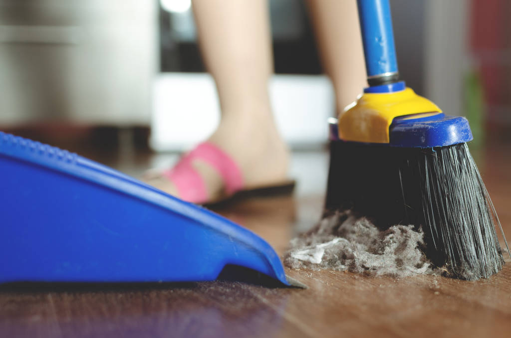 Woman is sweeping the floor by a sweeping brush from a dust. - Photo, Image