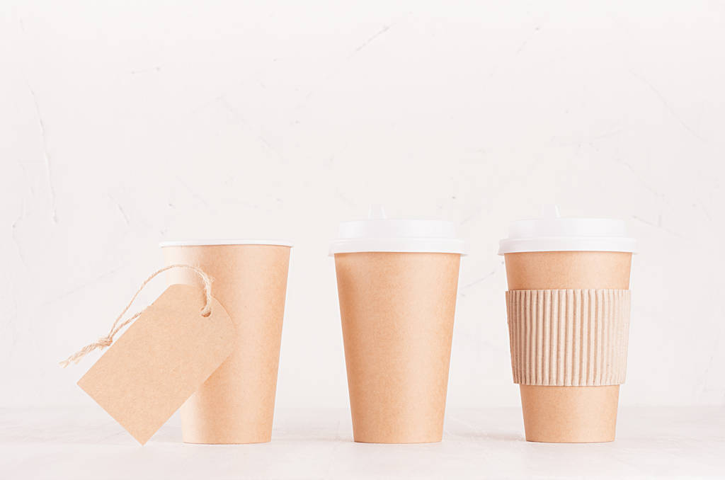 Макет для упаковки кави - набір з трьох ремісничих коричневих паперових чашок з білими шапками, тримачем чашок та порожньою етикеткою на дошці з білого дерева, інтер'єру кав'ярні. Сучасна елегантна концепція брендингу ідентичності, реклами, дизайну
. - Фото, зображення