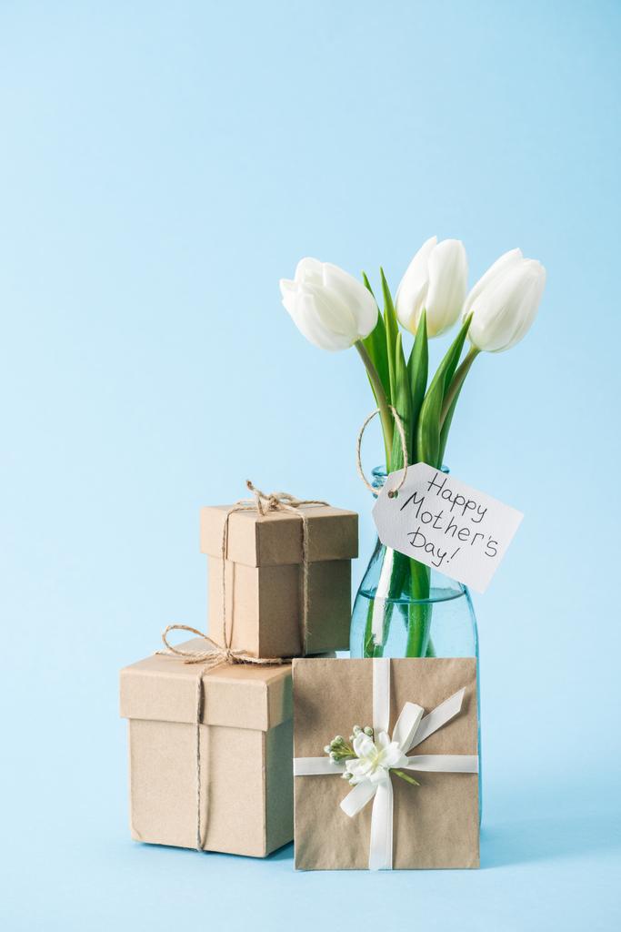 gift boxes, greeting card and bouquet of white tulips with happy mothers day greeting label on blue background - Photo, Image