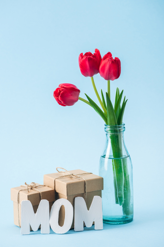 Dárkové krabičky, kytice červené tulipány a dokument white paper slovo máma na modrém pozadí - Fotografie, Obrázek