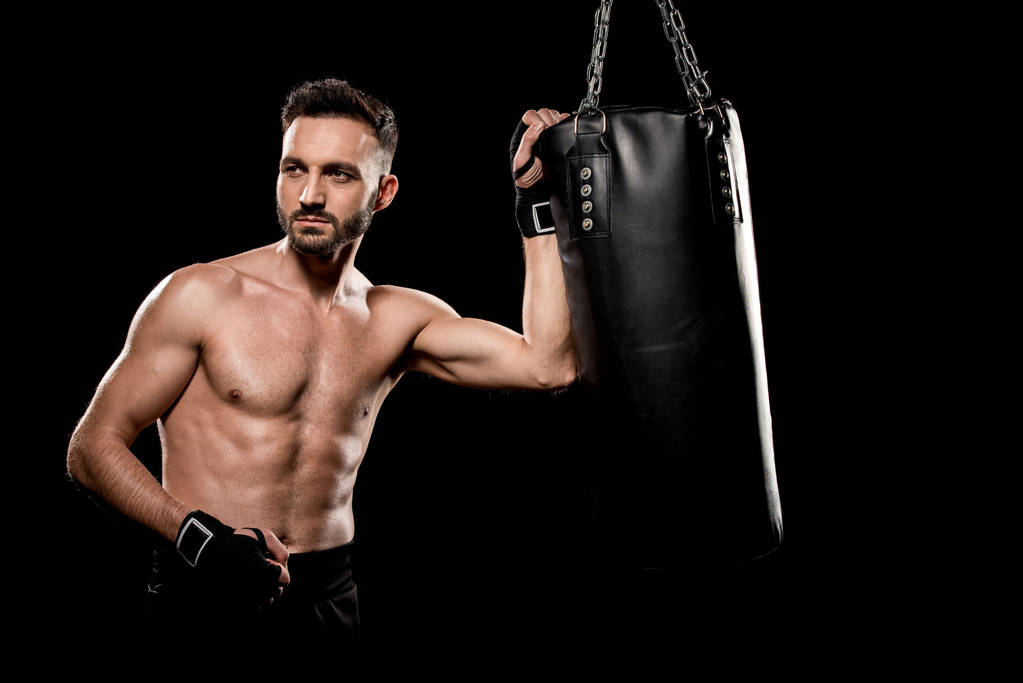 muskulöser, gutaussehender Boxer, der in der Nähe eines Boxsackes steht, isoliert auf schwarz - Foto, Bild