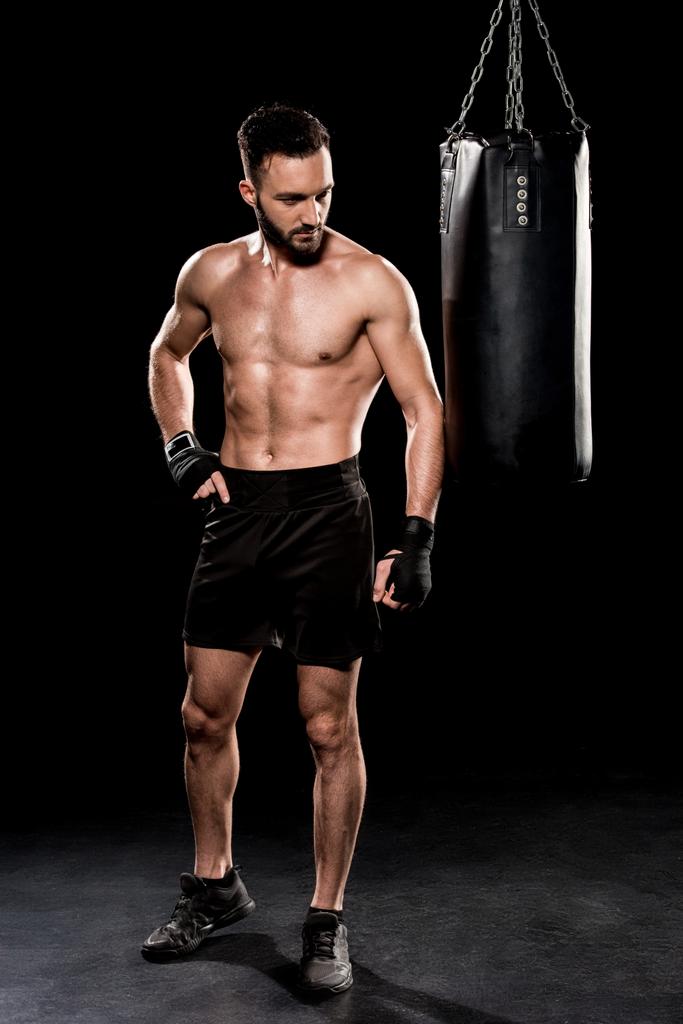 shortless bearded man looking at punching bag on black background - Photo, Image
