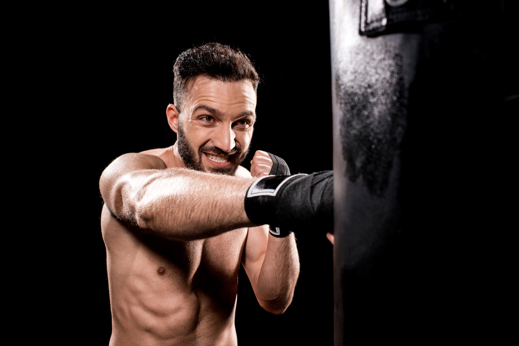 guapo sin cortocircuito deportista golpeando saco de boxeo aislado en negro
 - Foto, imagen