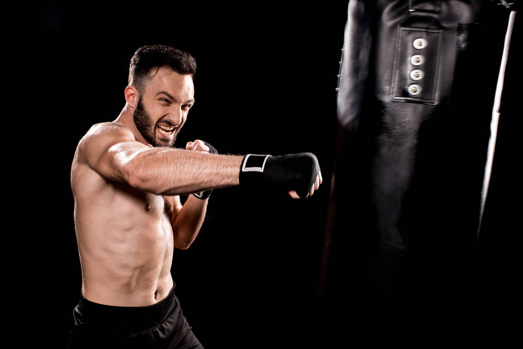 apuesto deportista patadas bolsa de boxeo aislado en negro
 - Foto, imagen