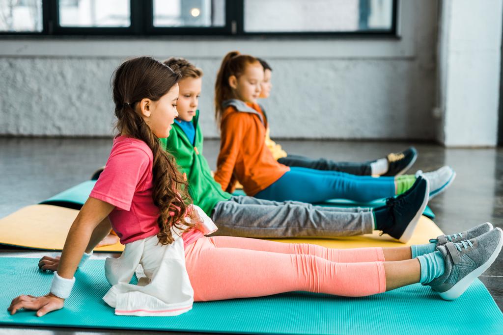 Preteen kids sitting on fitness mats and doing exercise - Photo, Image