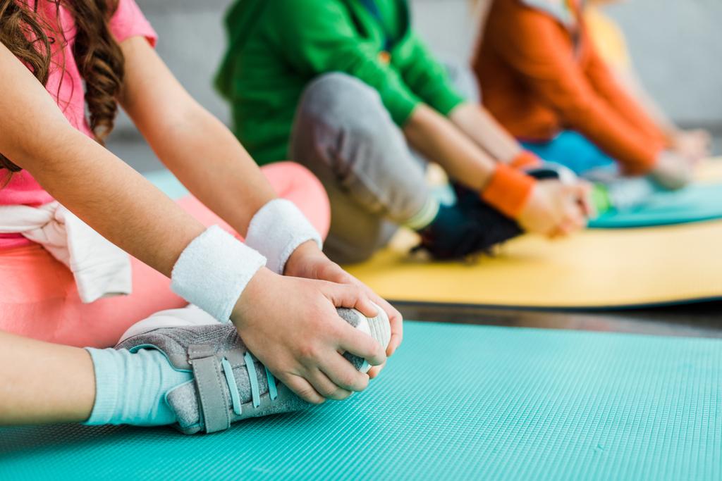 Обрезанный вид детей, растягивающихся на фитнес-ковриках
 - Фото, изображение