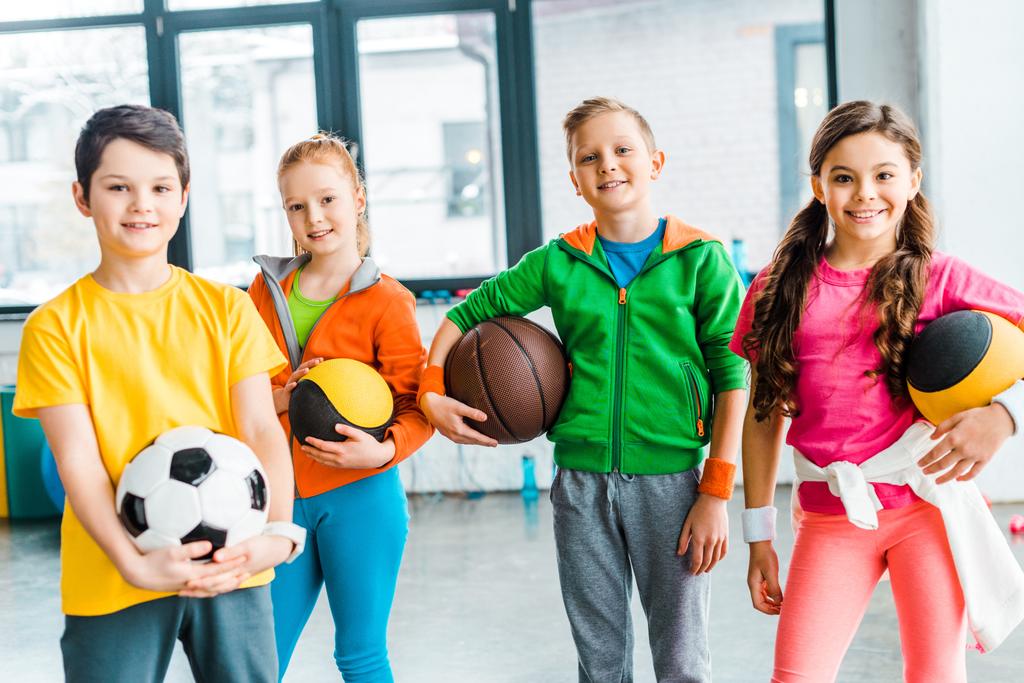 Беззаботные дети позируют с мячами в спортзале
 - Фото, изображение
