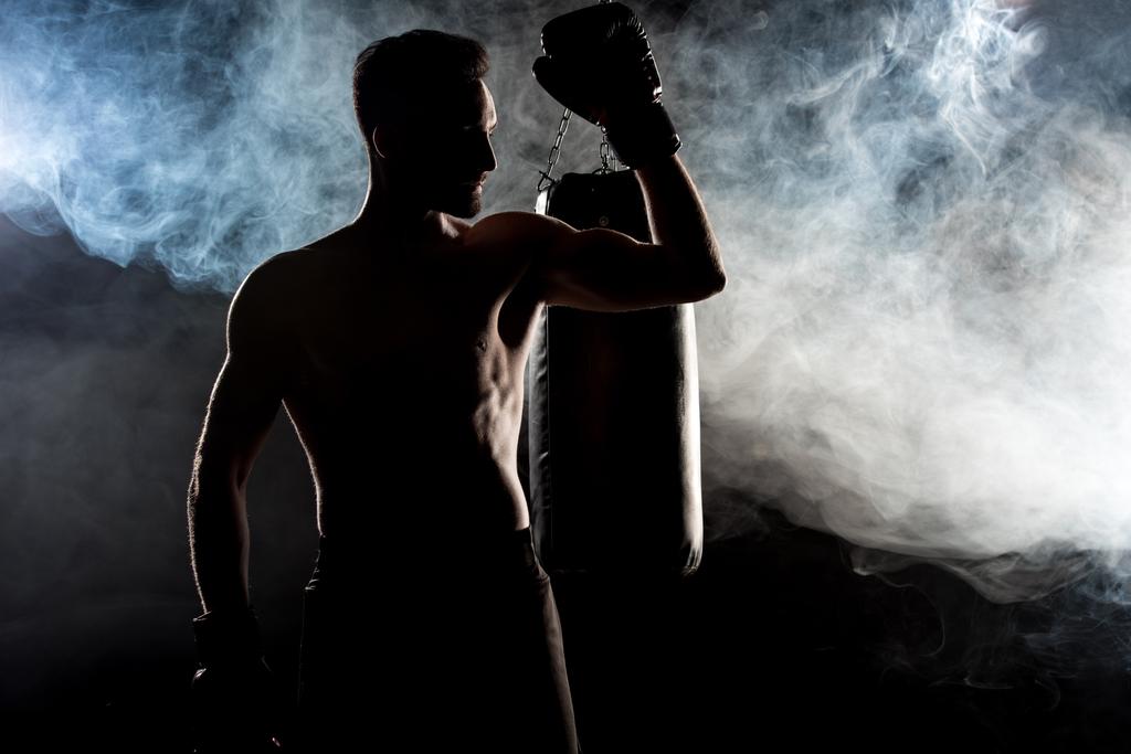 silhouet van gespierde sportman in bokshandschoenen op zwart met rook - Foto, afbeelding