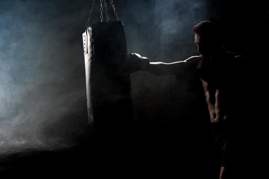 silhouette d'athlète musclé en gants de boxe donnant un coup de pied sac de boxe sur noir avec fumée
 - Photo, image