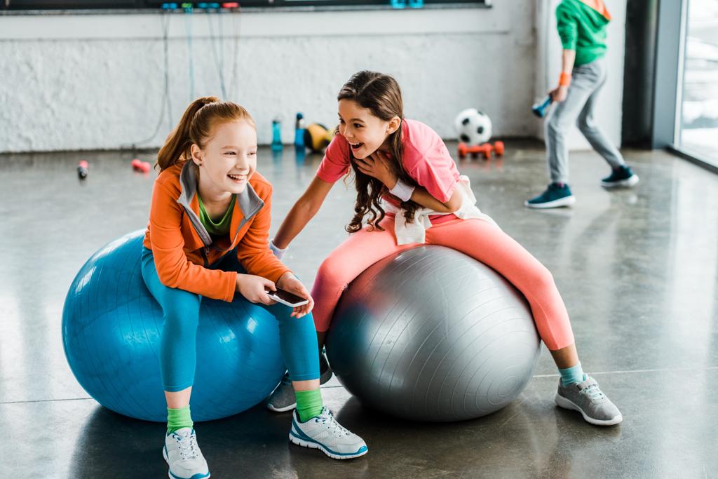 Smějící se děti s smartphone sedí na fitness míče - Fotografie, Obrázek