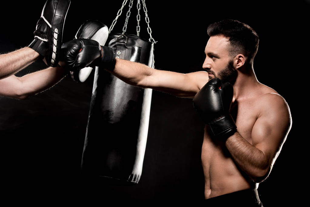 μυϊκή πυγμάχος αγωνίζεται με τον άνθρωπο σε διάτρηση γάντια που απομονώνονται σε μαύρο - Φωτογραφία, εικόνα