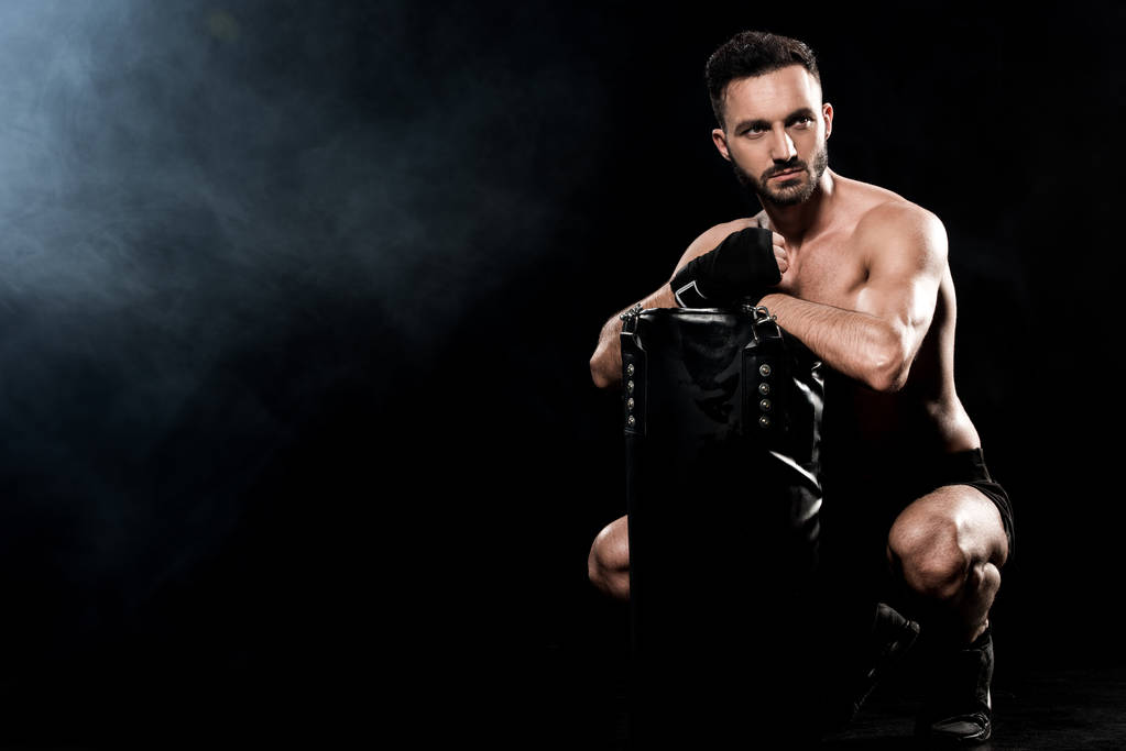 boxeur sans short assis et tenant sac de boxe sur noir avec de la fumée
 - Photo, image