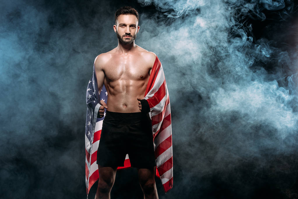 handsome athlete holding american flag on black with smoke - Photo, Image