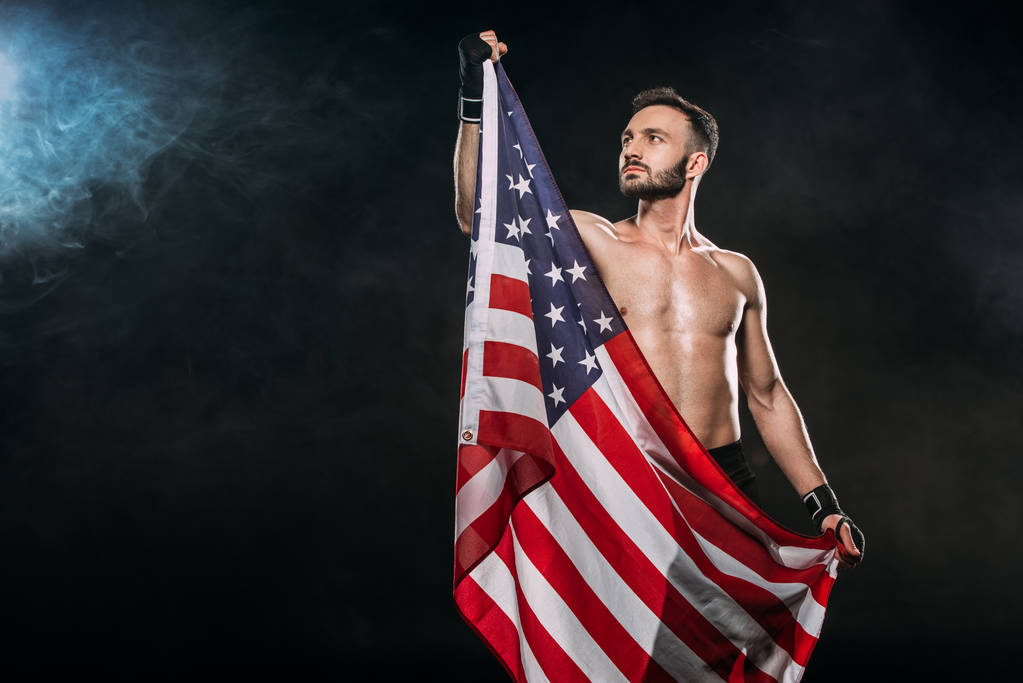 pohledný sportovec drží Americká vlajka na černém pozadí s kouřem - Fotografie, Obrázek