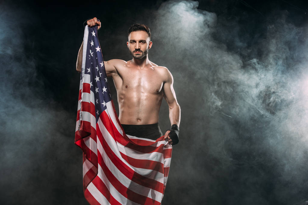 muscular man holding american flag on black with smoke - Photo, Image