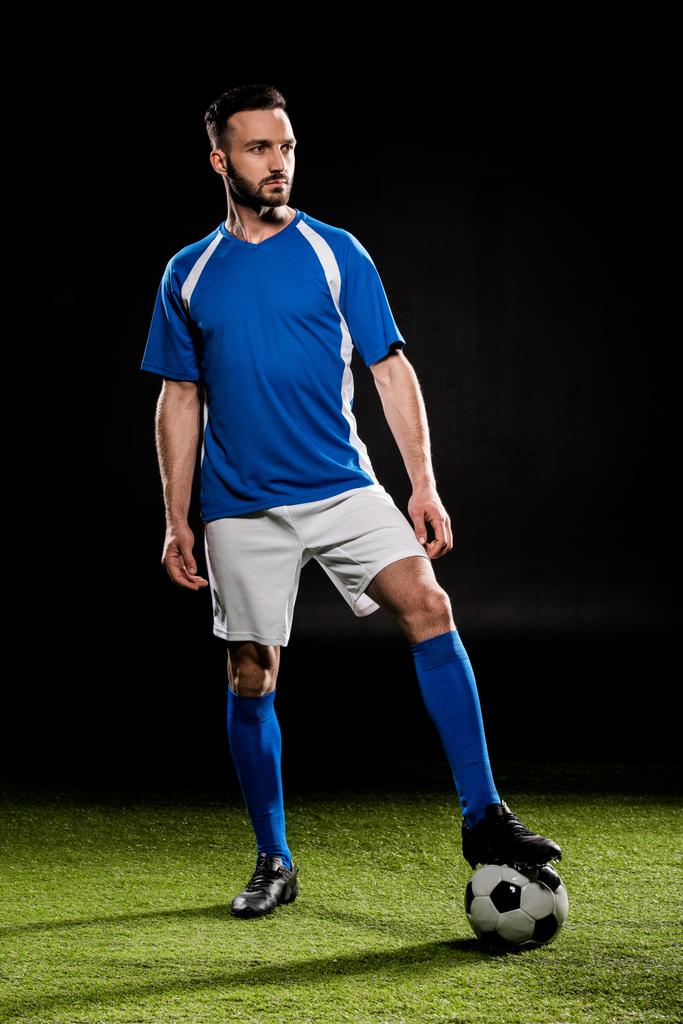 Brodaty piłkarz stojący z piłką na trawie, na czarnym tle - Zdjęcie, obraz