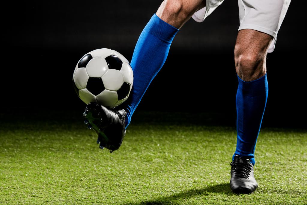обрезанный вид спортсмена, играющего с мячом на траве, изолированный на черном
 - Фото, изображение