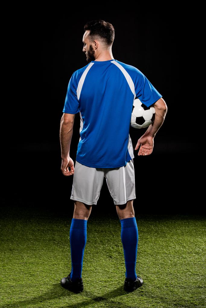 muscular sportsman in uniform holding ball isolated on black - Photo, Image