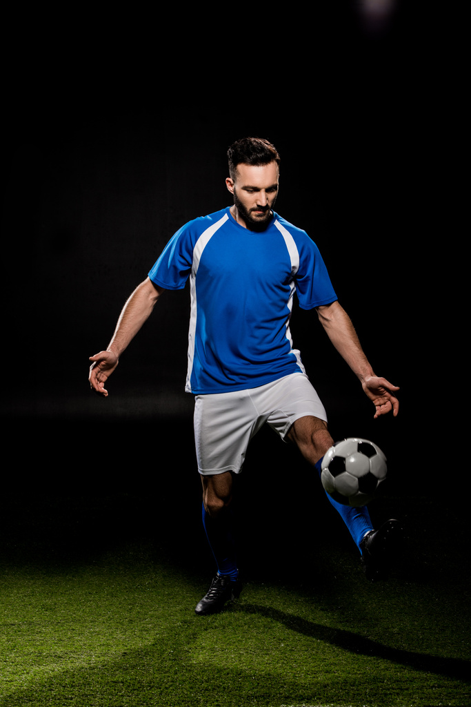 vousatý fotbalista v jednotné školení s míčem na trávě, samostatný na černém - Fotografie, Obrázek