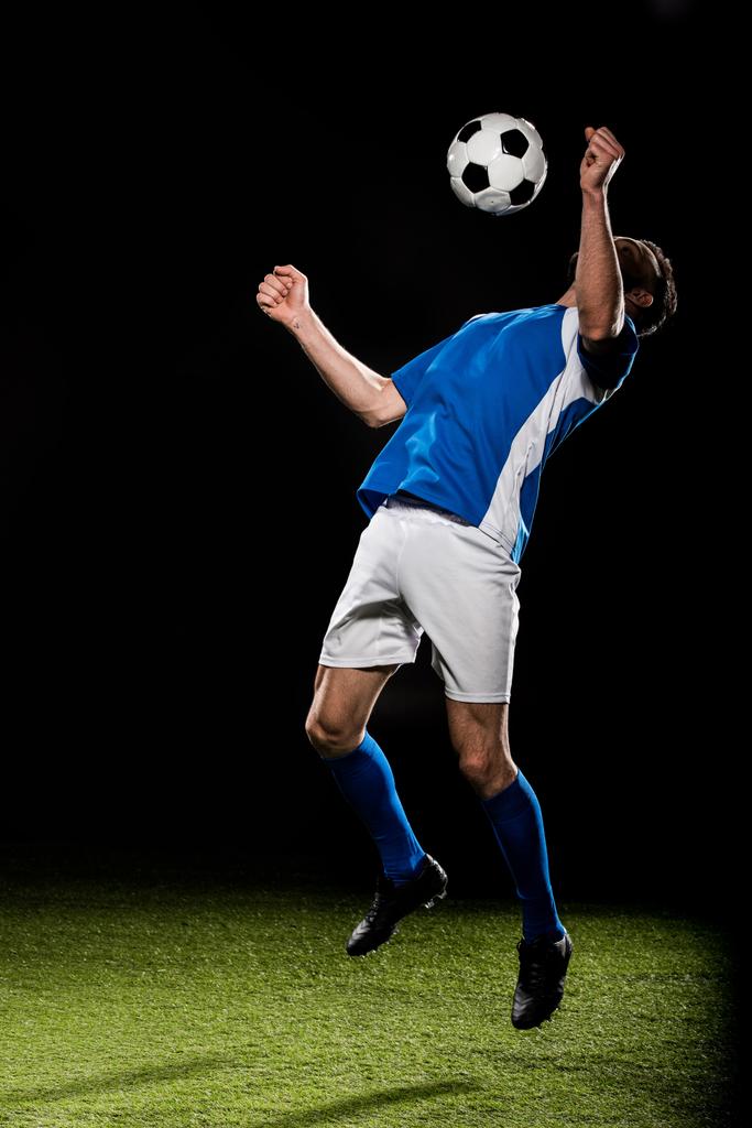 bebaarde football-speler in uniform springen met bal geïsoleerd op zwart - Foto, afbeelding