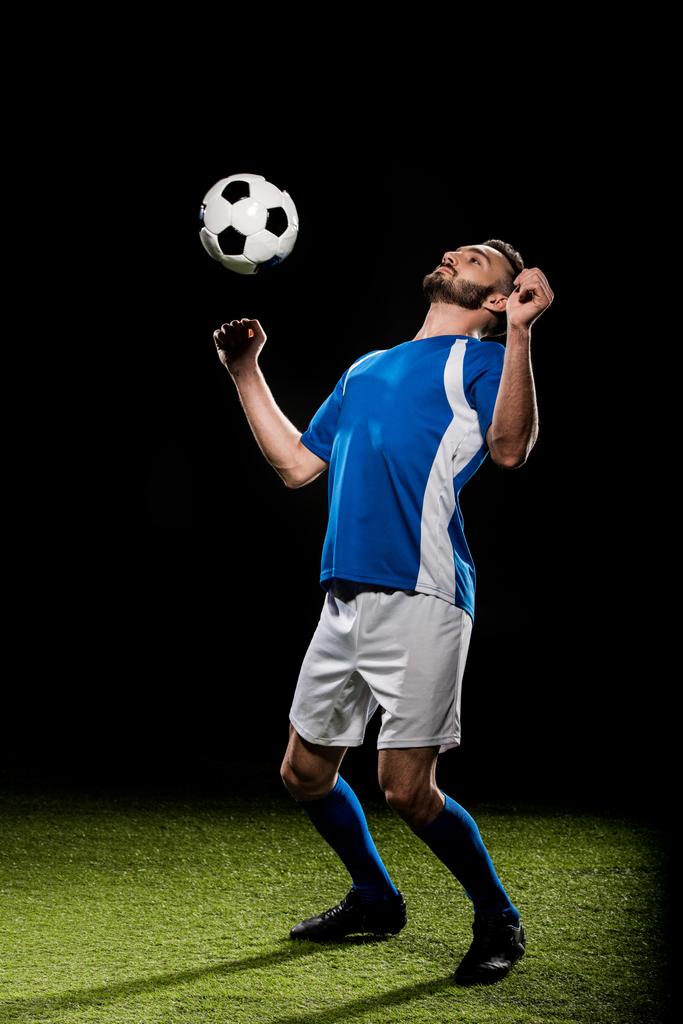 guapo jugador de fútbol en uniforme de entrenamiento con pelota en hierba aislado en negro
 - Foto, Imagen