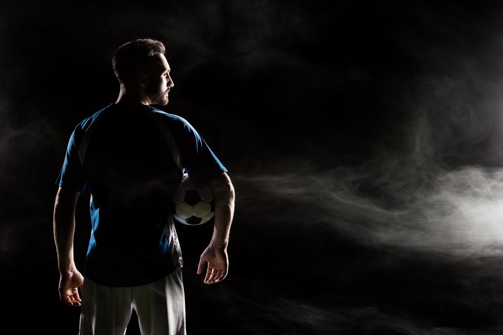 煙と黒のボールを保持しているフットボール選手のシルエット   - 写真・画像