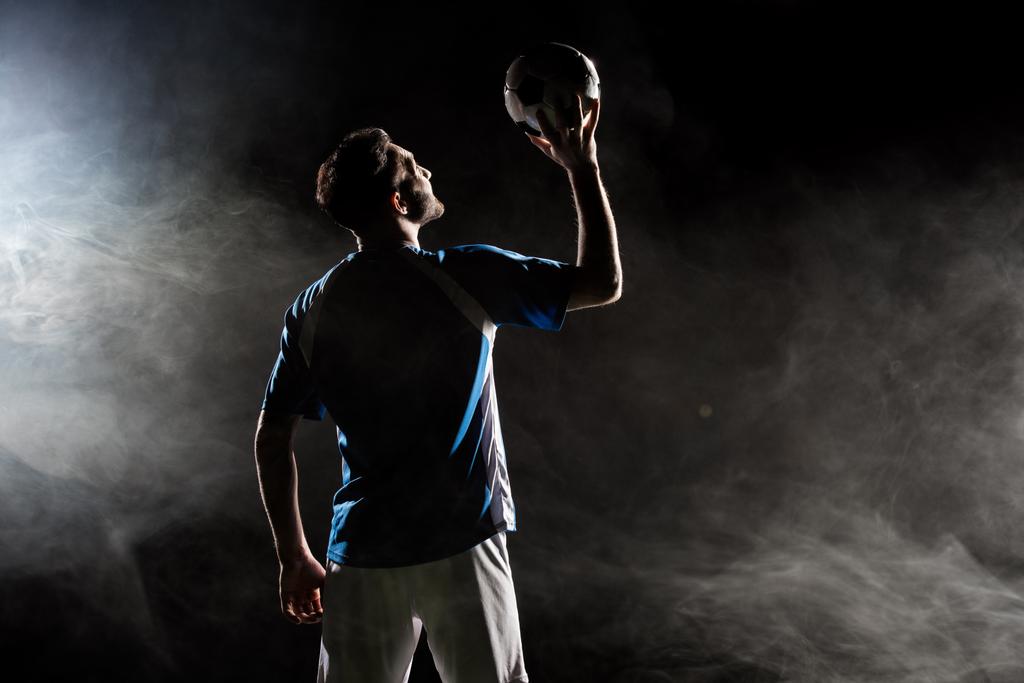 silueta del jugador en uniforme sosteniendo la bola por encima de la cabeza en negro con humo
   - Foto, Imagen