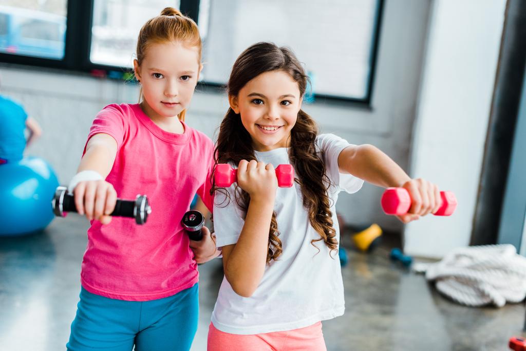 Active kids doing exercise with dumbbells in gym - Photo, Image