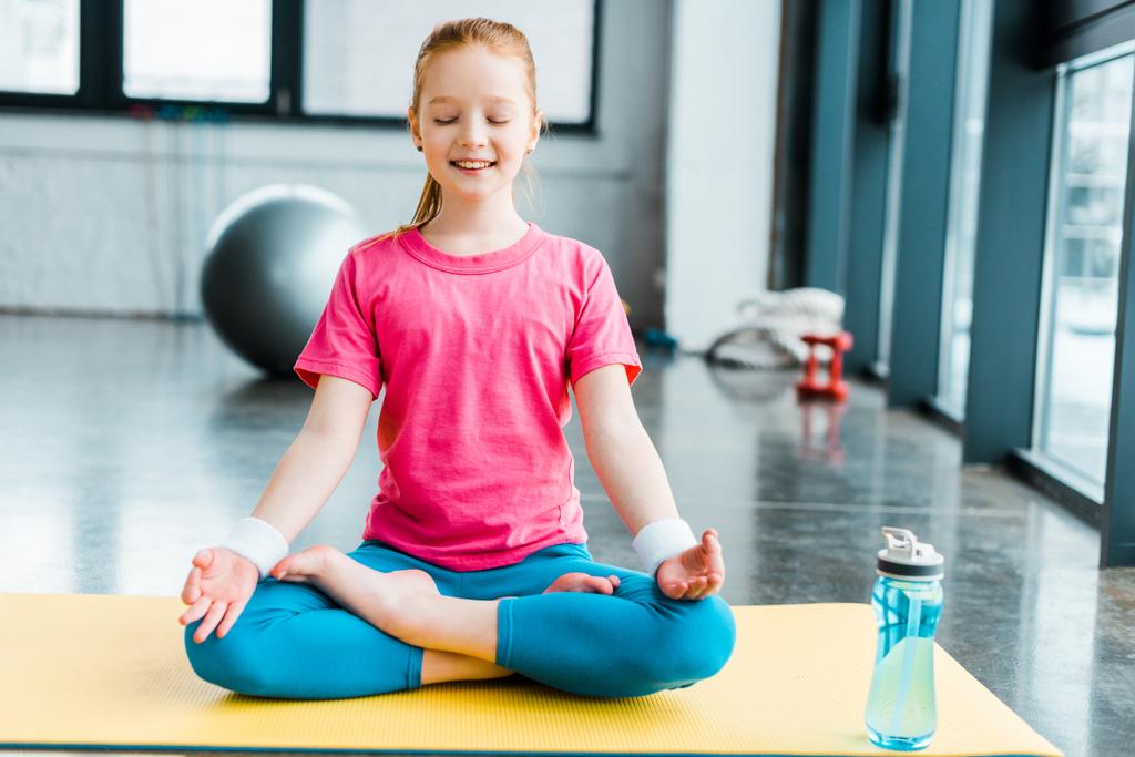 Ginger kid practicing yoga and sitting in lotus pose with closed eyes - Photo, Image