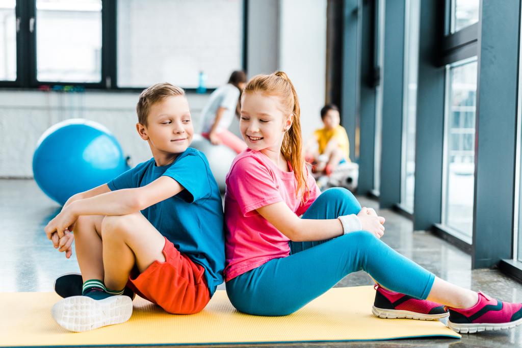 Δυο παιδιά κάθονται πλάτη με πλάτη σε γυμναστήριο χαλί - Φωτογραφία, εικόνα