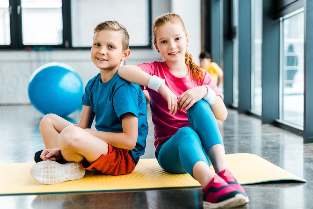 Preteen friends sitting on fitness mat in gym - Photo, Image