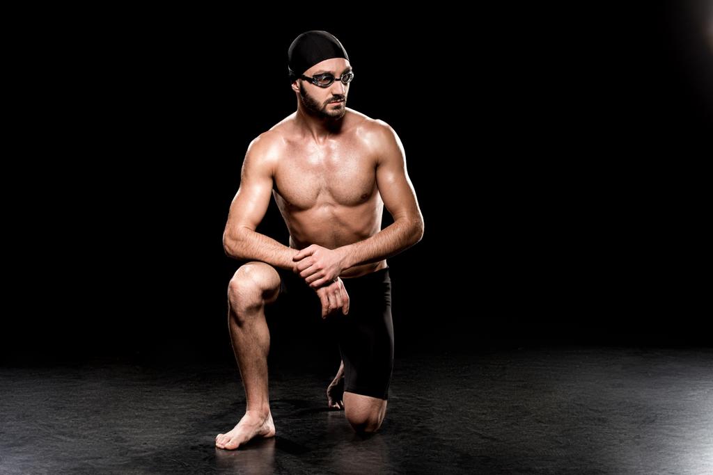 athletic man sitting in swimming cap and goggles on black background - Photo, Image