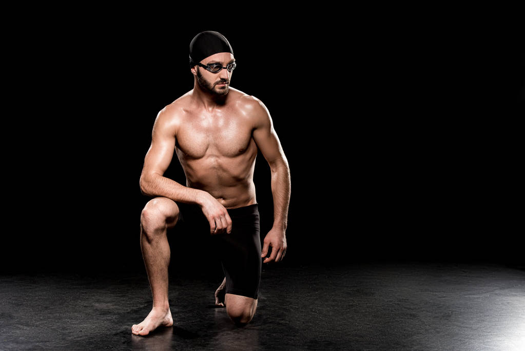 atletico sportivo seduto in cuffia da nuoto e occhiali su sfondo nero
 - Foto, immagini