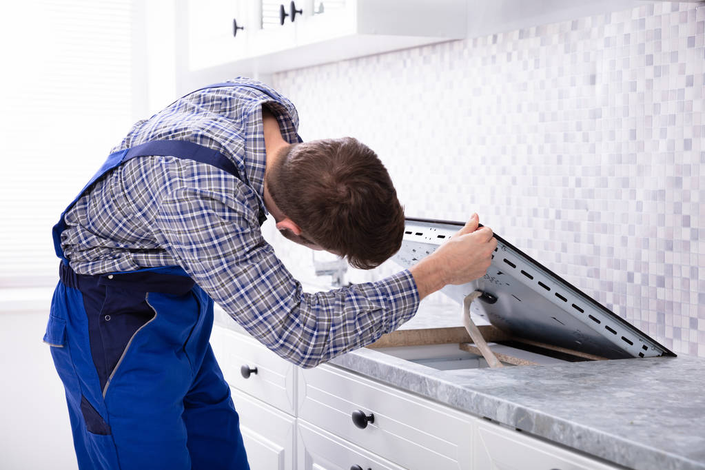 Jonge reparateur installeren inductie fornuis In de keuken - Foto, afbeelding