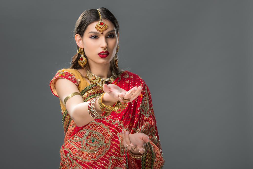Indianerin gestikuliert in traditionellem Sari und Accessoires, isoliert auf grau  - Foto, Bild