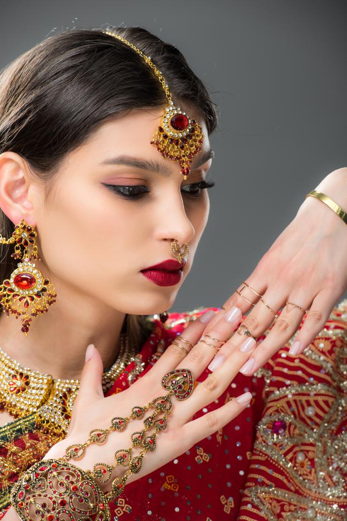 attraktive indische Frau gestikuliert in traditionellen Accessoires, isoliert auf grau  - Foto, Bild