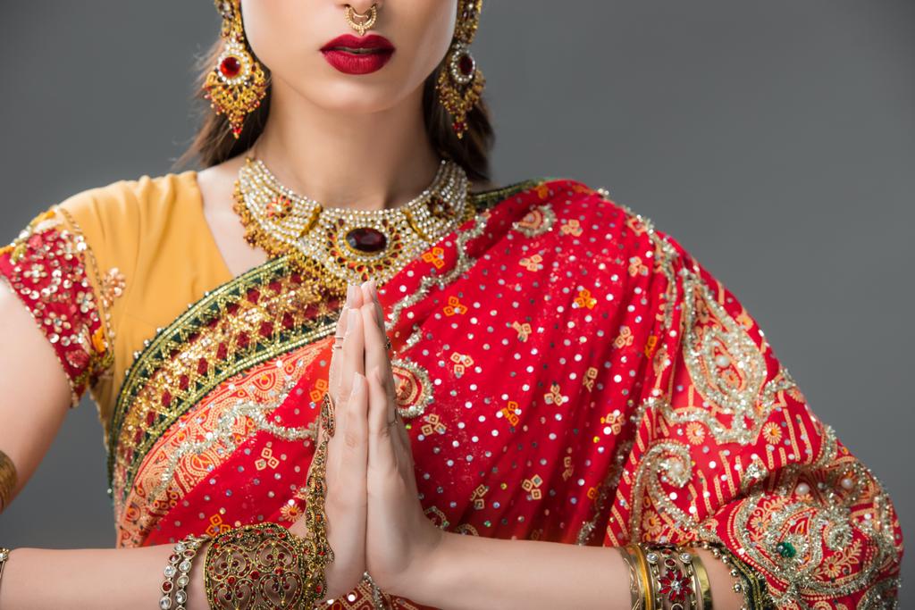 обрезанный вид индийской женщины в традиционной одежде с мудрой намасте, изолированный на сером
  - Фото, изображение