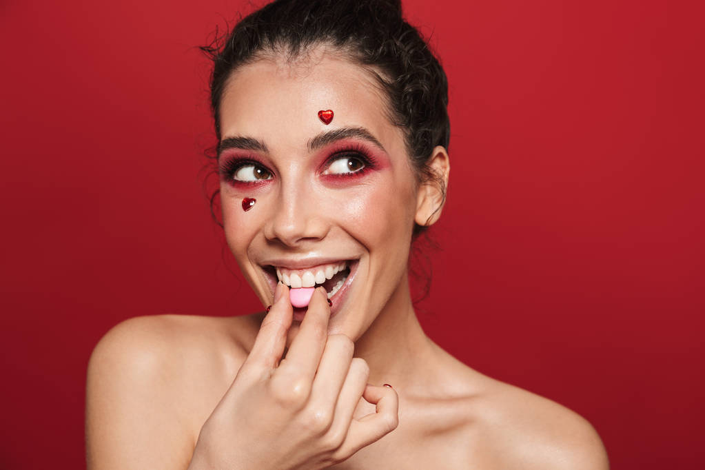 Красота портрет привлекательной молодой топлесс женщина с макияжем стоя изолированы на красном фоне, едят конфеты
 - Фото, изображение
