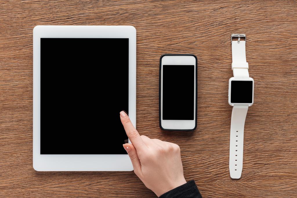 Vista cortada de mulher com tablet digital, smartphone e smartwatch com tela em branco no fundo de madeira
 - Foto, Imagem