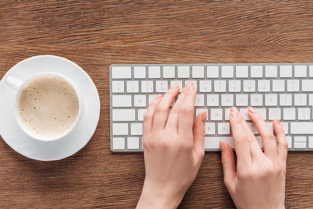 Обрезанный вид девушки, печатающей на клавиатуре на деревянном фоне
 - Фото, изображение