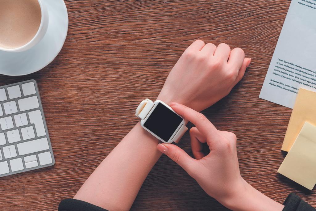 Vue recadrée de la fille en utilisant smartwatch avec écran blanc sur fond en bois
 - Photo, image